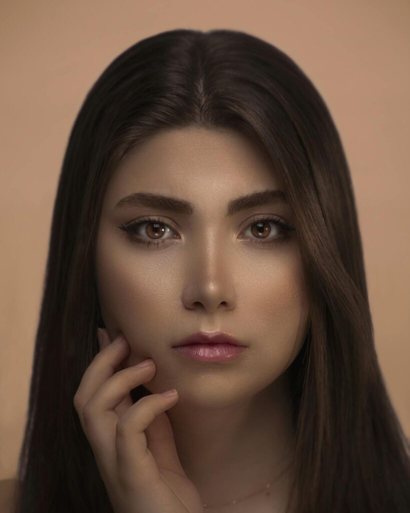 Close-up portrait of a woman with brown eyes, natural makeup, and touching her face.